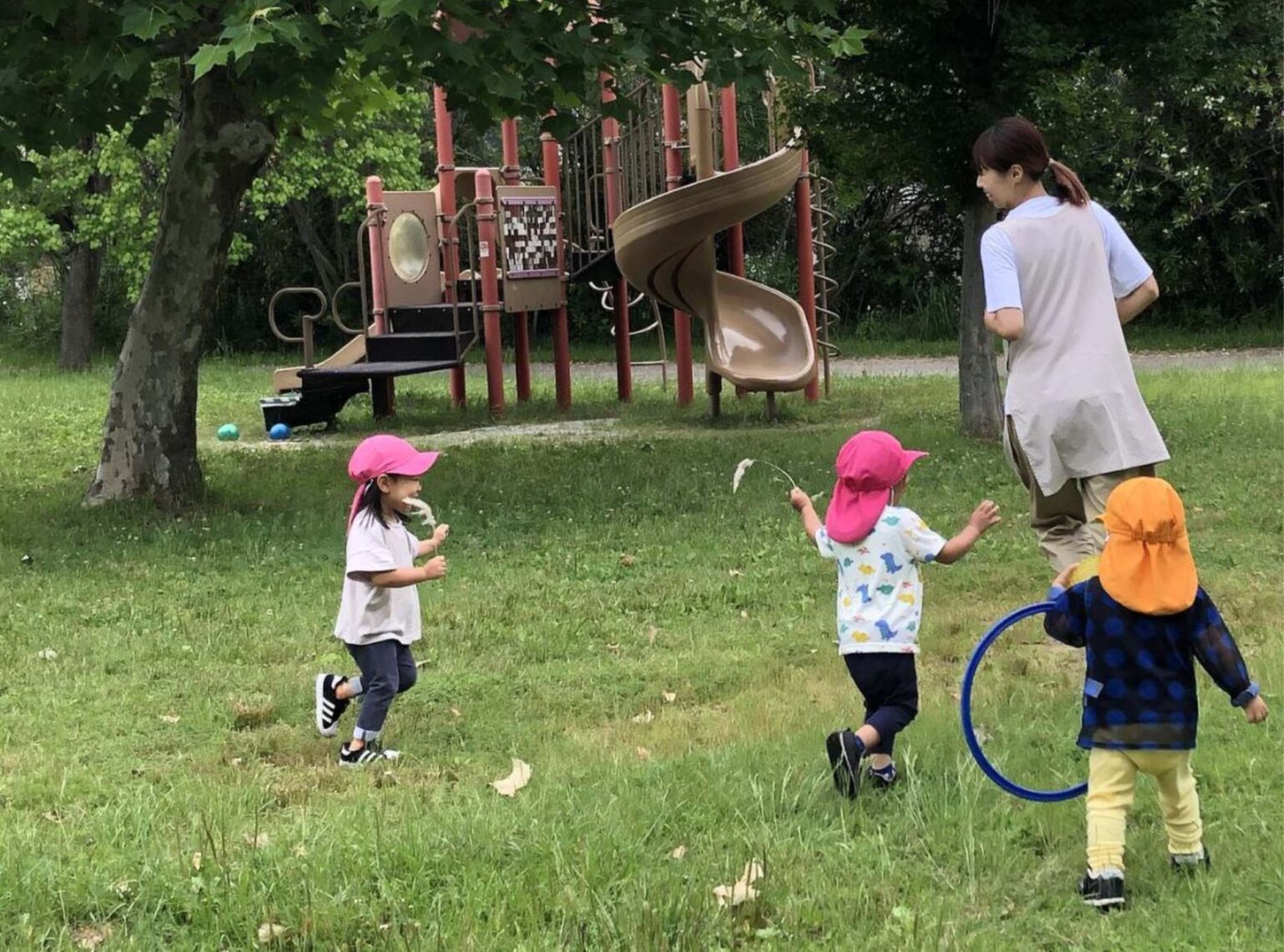 緑の公園でのびのび遊ぶ子どもたちと保育士